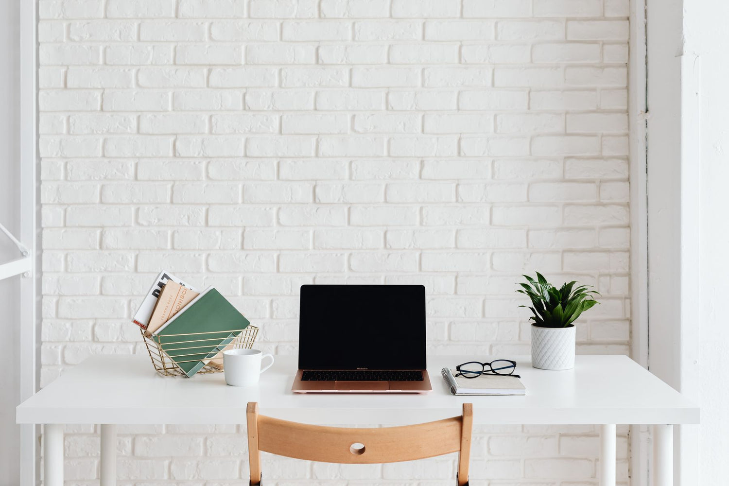 Opgeruimd wit bureau met een laptop en een kleine plant in een witte pot